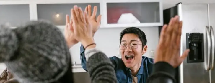 A diverse group of adults sharing a celebratory high five in a modern kitchen setting.