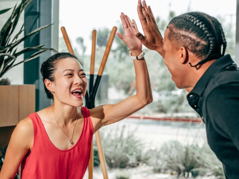 Excited coworkers giving a high five, symbolizing teamwork and success in a modern office setting.